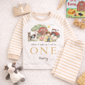 Personalised farm themed birthday pyjamas with beige striped sleeves and trousers, featuring barnyard animals and the text “When I wake up I will be one Harry”, displayed in a farm themed flat lay on a fluffy background.